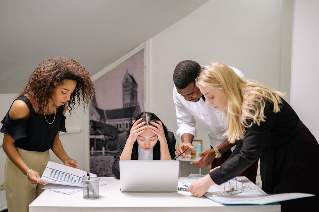 Diverse group of coworkers engaged in a collaborative office meeting, discussing around a laptop.